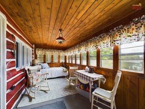 L’intérieur d’une cabane comprenant un lit, un fauteuil à bascule, une table et des fenêtres donnant sur un paysage naturel.