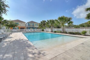 Ein Swimmingpool mit weißem Zaun, Liegestühlen und blauem Himmel.