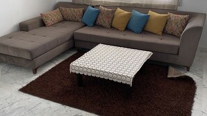 A living room with a sectional sofa, patterned cushions, a patterned ottoman, and a brown rug. - THE GOOD ADRESS (Ariana)