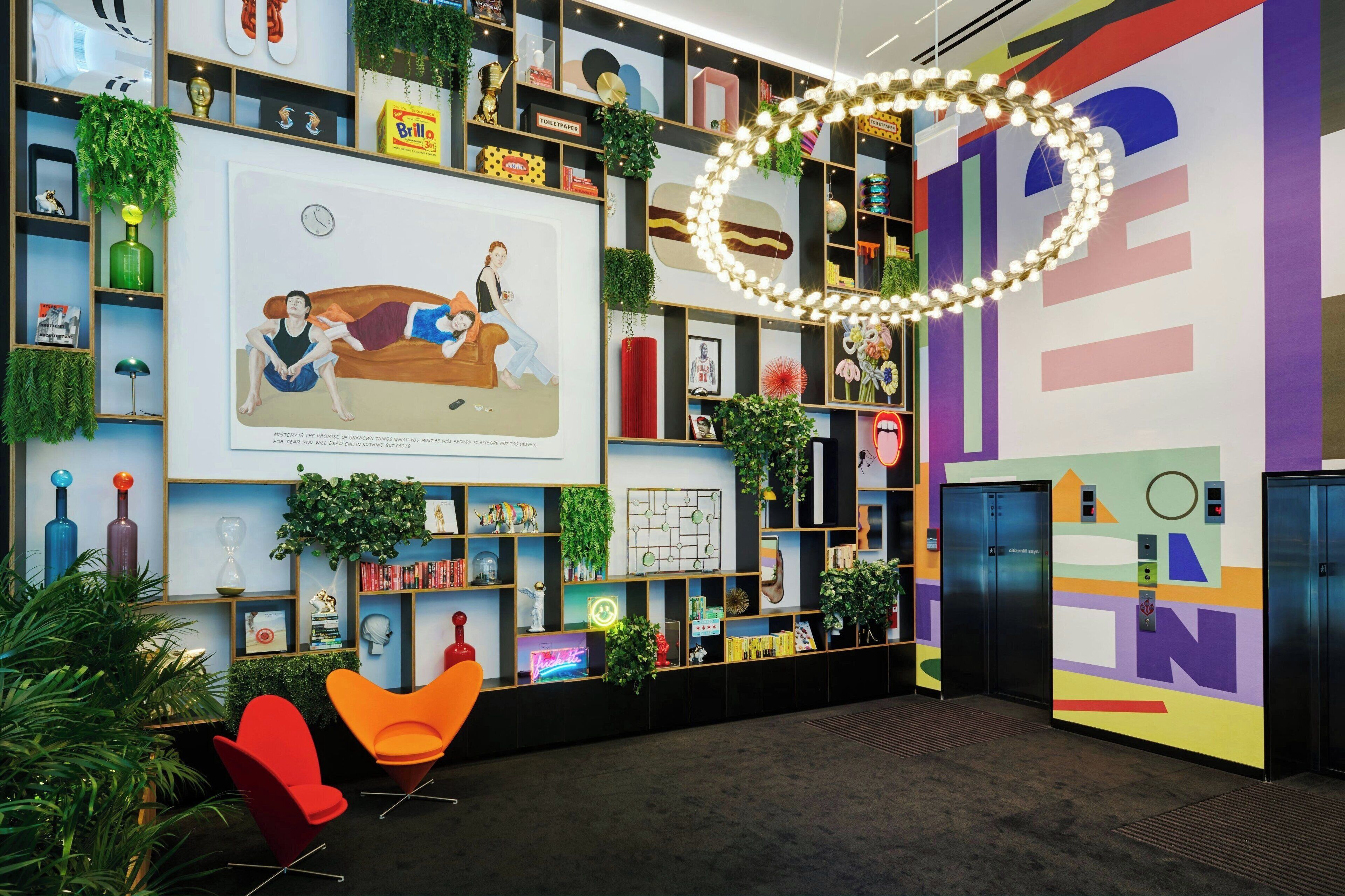 Um lobby moderno com uma parede colorida, prateleiras com diversos objetos e uma grande obra de arte retratando duas pessoas.