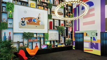 Een moderne lobby met een kleurrijke wand, planken met diverse objecten en een groot kunstwerk waarop twee personen te zien zijn.