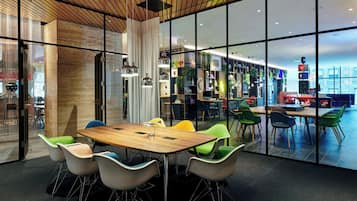 A modern conference room with a wooden table and colorful chairs, large windows, and a view of a restaurant area.