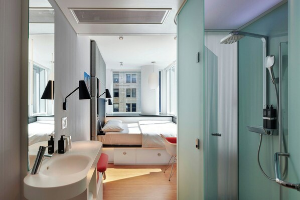 A modern hotel room with a large bed, a bathroom with a shower, and a view of a cityscape.