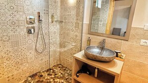 A bathroom with patterned tiles, a glass-enclosed shower, a stone sink, and a wooden ceiling.