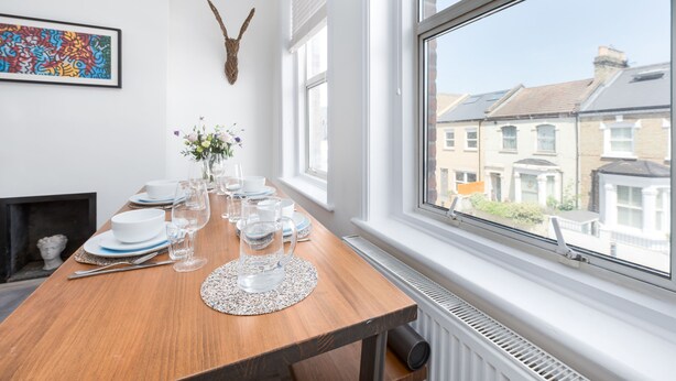 Ein Essbereich mit Holztisch, gedecktem Tisch, Kamin, großem Fenster mit Blick auf Gebäude und einem farbenfrohen abstrakten Gemälde an der Wand.