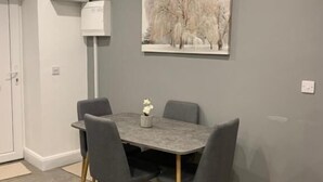 Un comedor con una mesa y sillas grises, un cuadro de árboles y una pared blanca.