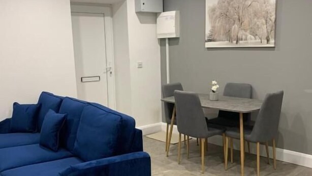 Una sala de estar con un sofá azul, una mesa de comedor con sillas, una puerta y un aire acondicionado instalado en la pared.