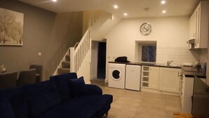 Un espacio habitable compacto con sofá, lavadora, lavamanos y una escalera que conduce a un nivel superior.