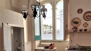 Uma área de refeições com mesa e cadeiras de madeira, luminária pendente, janela com vista e cozinha com pia e armários.