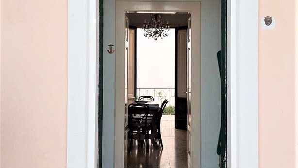 Uma porta em arco dá acesso a uma sala de jantar com um candelabro acima.