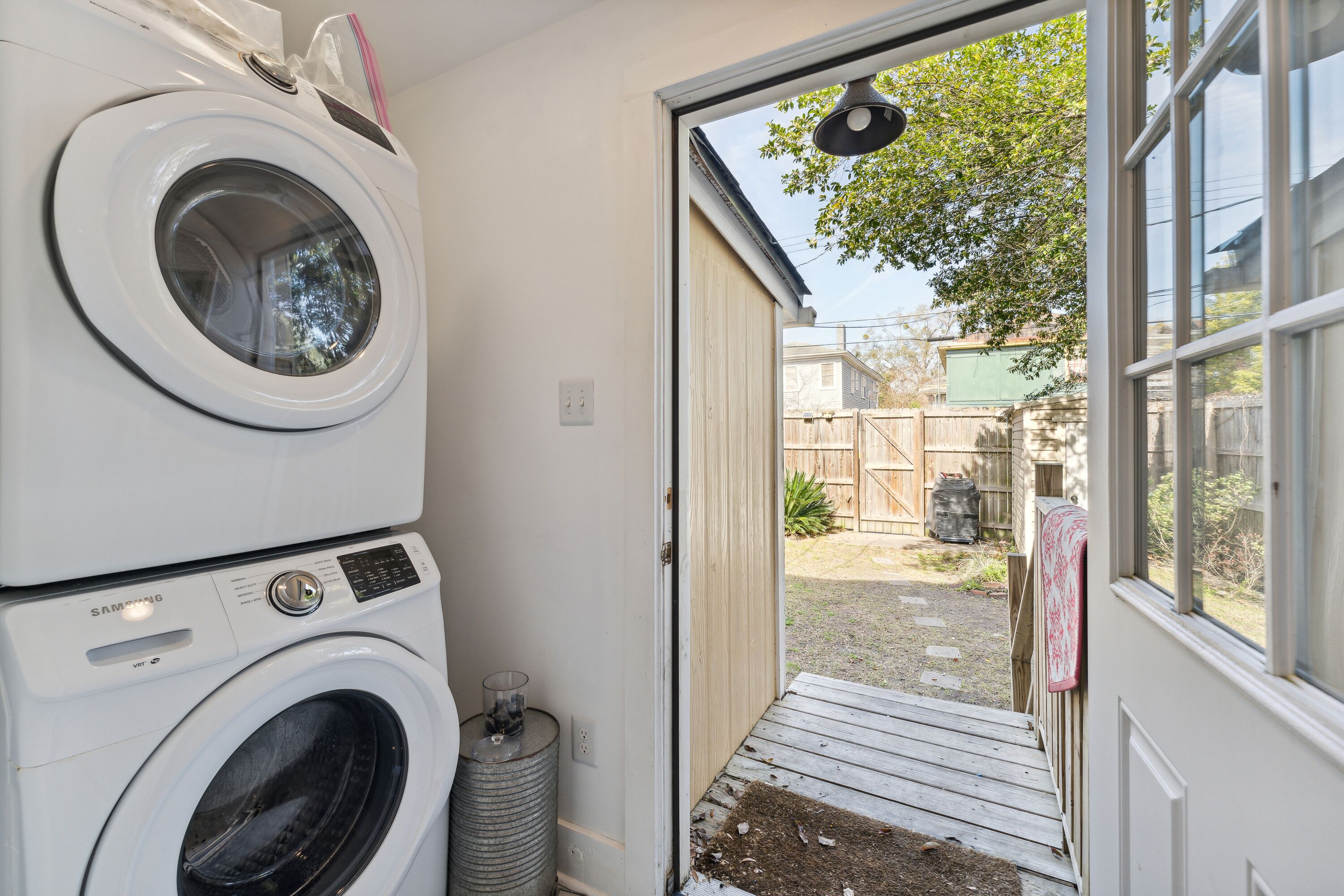 A laundry room with two stacked washers and dryers, a trash can, and a door leading to a backyard.