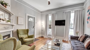 Una sala de estar con chimenea, sillones verdes, un sofá oscuro y un televisor de pantalla plana.