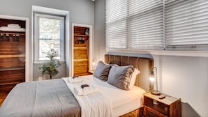 Un dormitorio moderno con una cama grande, estanterías de madera, una planta en maceta y una ventana con persianas.