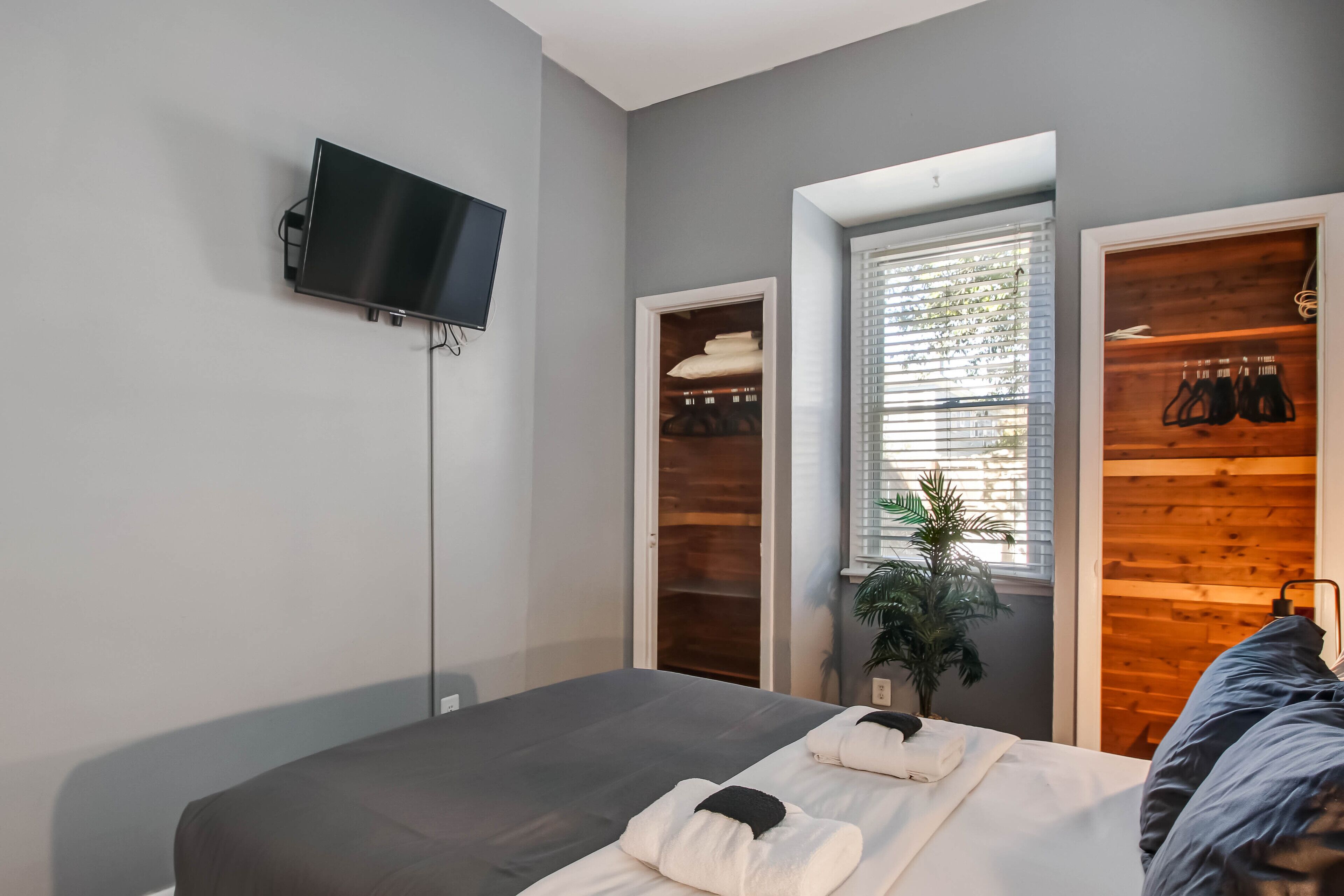 Quarto de hotel moderno com cama, televisão na parede, janela com persianas e armário de madeira.