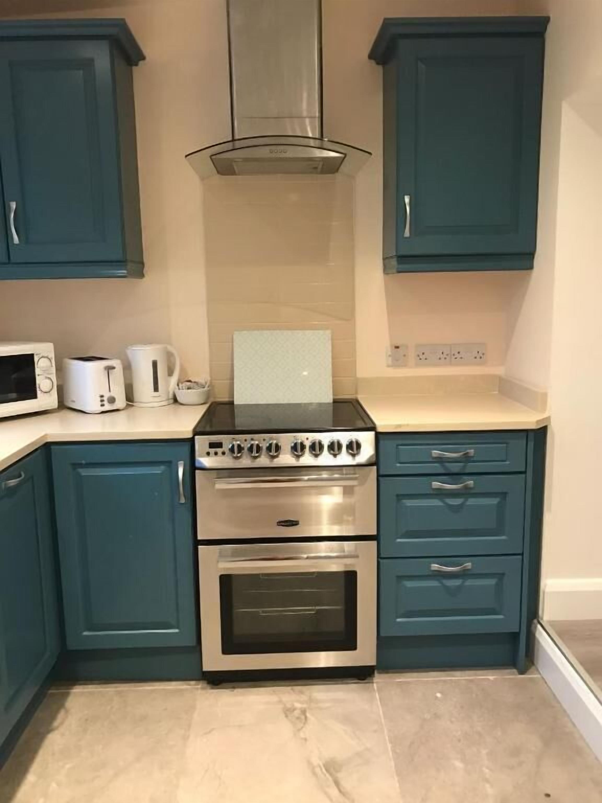 A kitchen with teal cabinets, a stainless steel range hood, a microwave, a toaster, and a coffee maker.
