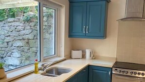 A kitchen with teal cabinets, a built-in oven, and a window overlooking a stone wall. - 6 Eyre Square Lane (Galway)