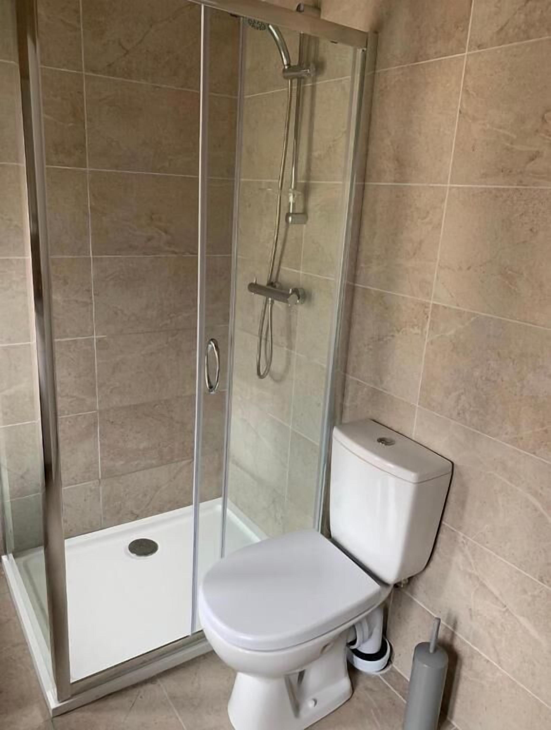 A bathroom with a glass-enclosed shower, a white toilet, and beige tiled walls.