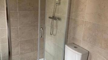 A bathroom with a glass-enclosed shower, a white toilet, and beige tiled walls.