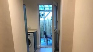 A hallway with a washing machine, a chair, and a door leading to an outdoor area. - 6 Eyre Square Lane (Galway)