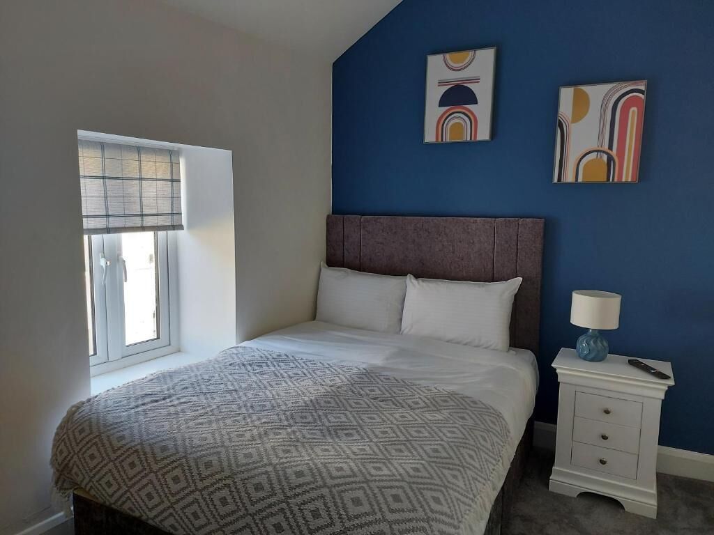 Ein Schlafzimmer mit einem Bett, einem Nachttisch, einer Lampe und zwei abstrakten Bildern an der Wand.
