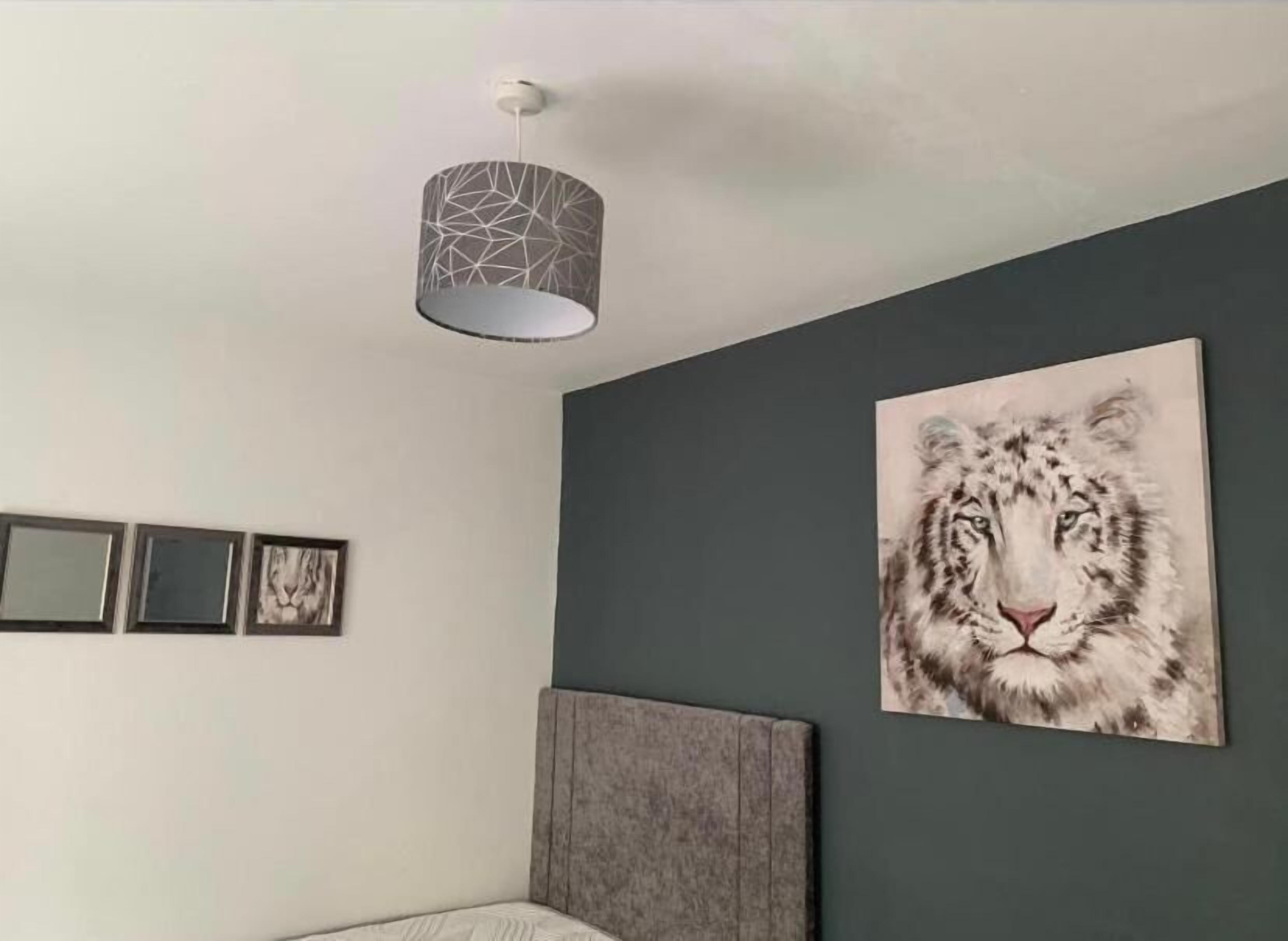A bedroom with a grey wall, a large framed picture of a snow leopard, a grey headboard, and a hanging light fixture.