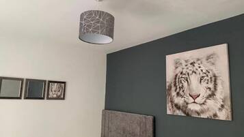 A bedroom with a grey wall, a large framed picture of a snow leopard, a grey headboard, and a hanging light fixture.