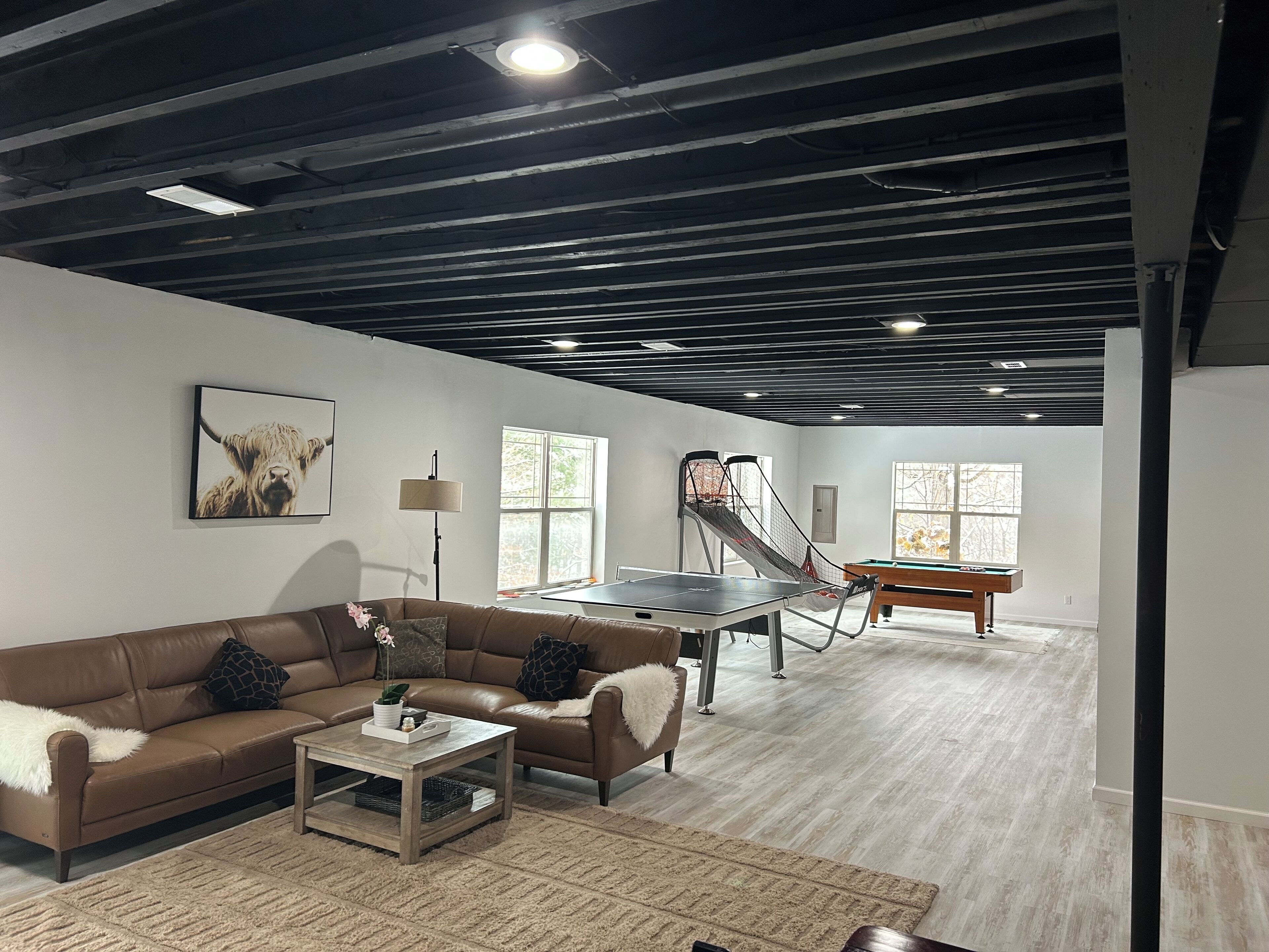 A spacious living room with a brown leather sofa, a coffee table, and a ping pong table.