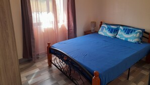 A bedroom with a bed, curtains, a nightstand, and a wall-mounted light. - GINGER ACCOMMODATION + POOL (Trou aux Biches)