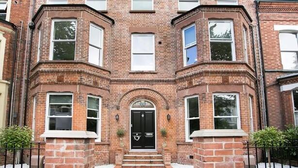 A brick townhouse with a black front door, multiple windows, and a small front garden.