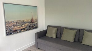 A living room with a gray sofa and a large cityscape painting of the Eiffel Tower.