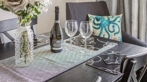 A dining table with a bottle of Prosecco, two wine glasses, and a patterned placemat.