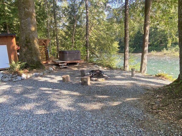 Un espace recouvert de gravier avec un foyer, une terrasse en bois et un jacuzzi.