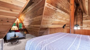 A cozy attic bedroom with wooden walls, a bed, a small table with a lamp, and a window with a view. - Small Timbers-riverfront log home, stunning view (Gold Bar)
