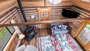 A cozy cabin interior with a sofa, a fireplace, a television, and a patterned rug. - Small Timbers-riverfront log home, stunning view (Gold Bar)
