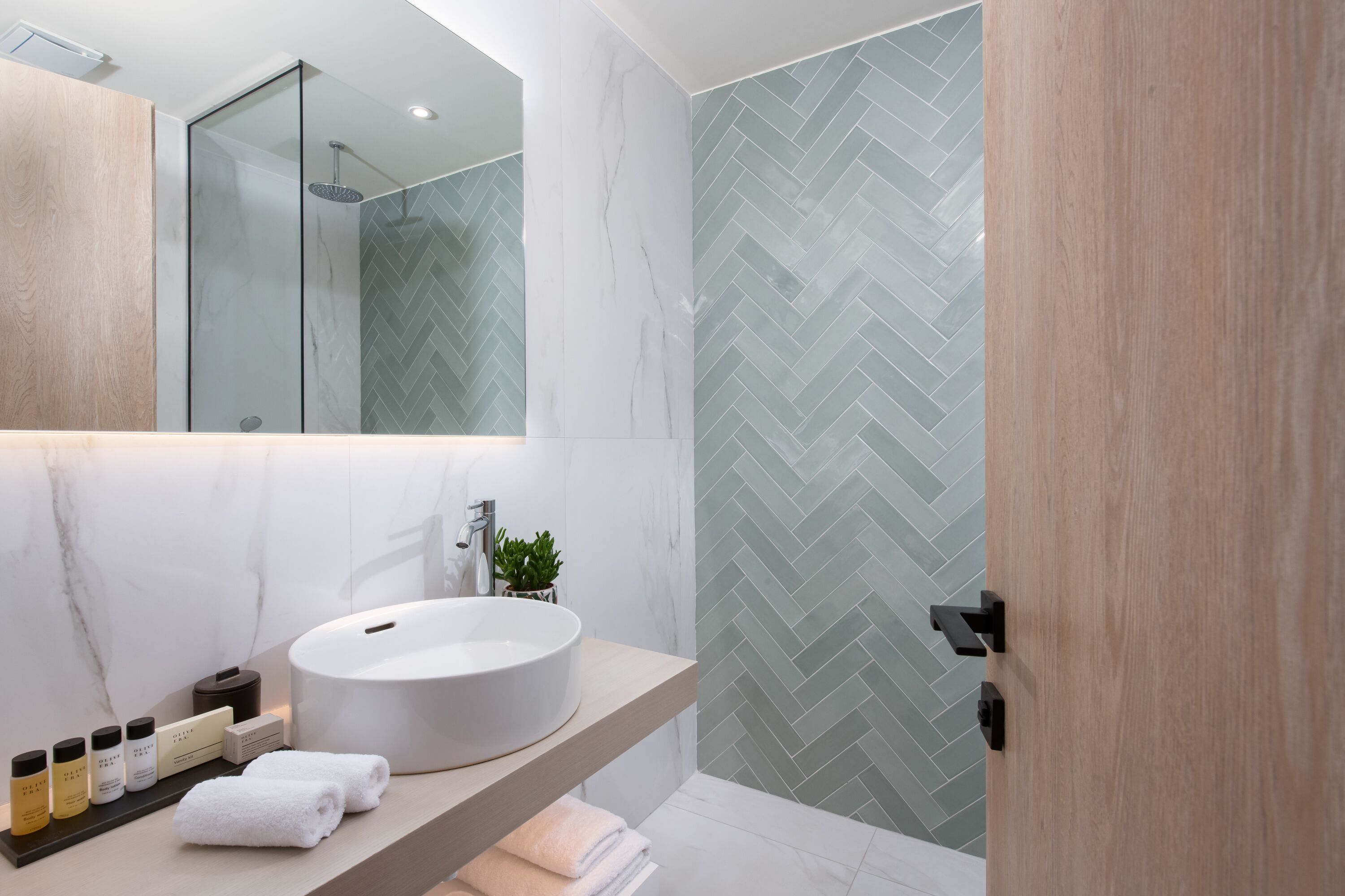Un baño moderno con un lavabo redondo, un espejo y un revestimiento de ducha con motivo de espiga.