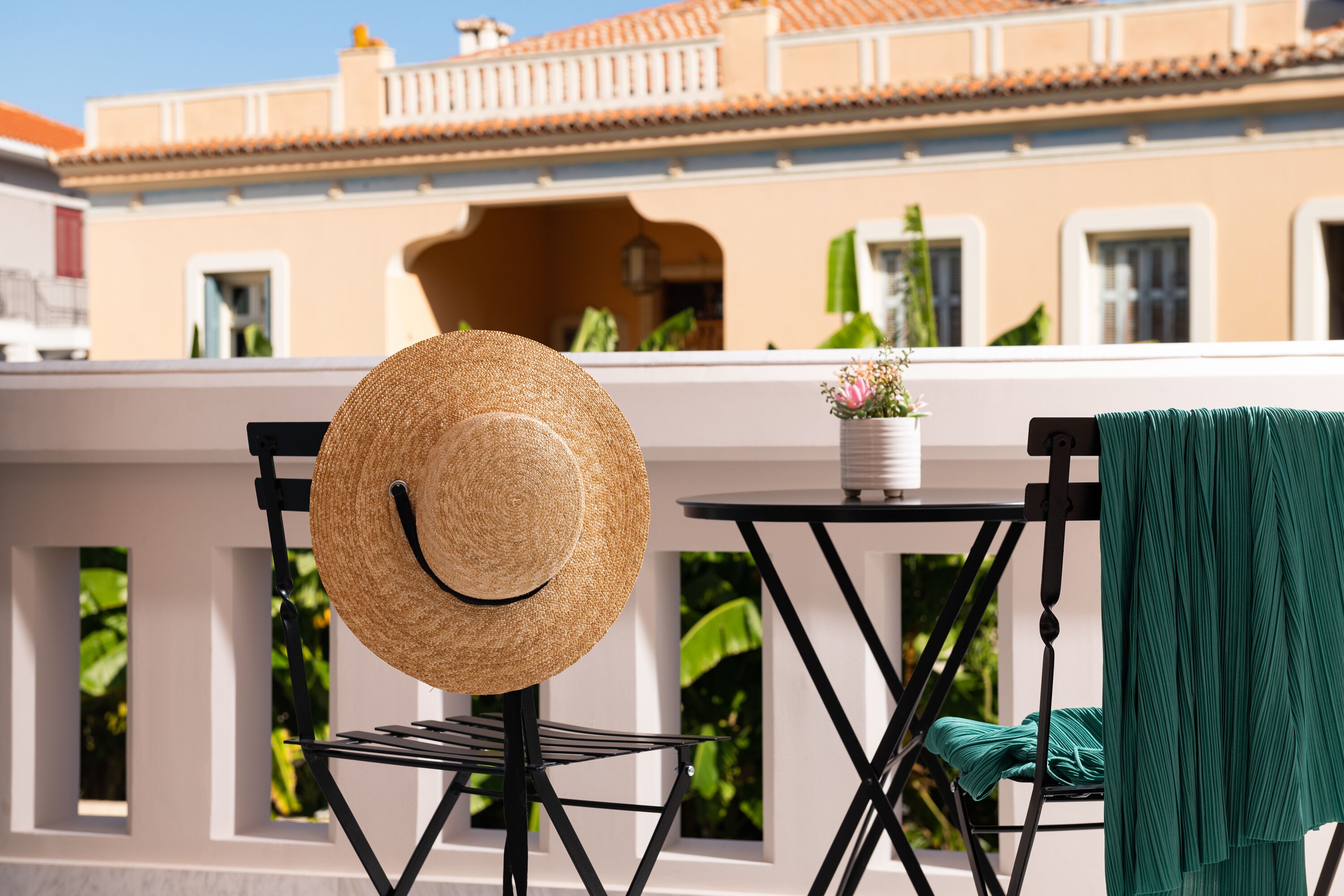 A balcony with a wicker chair, a table, and a green towel.