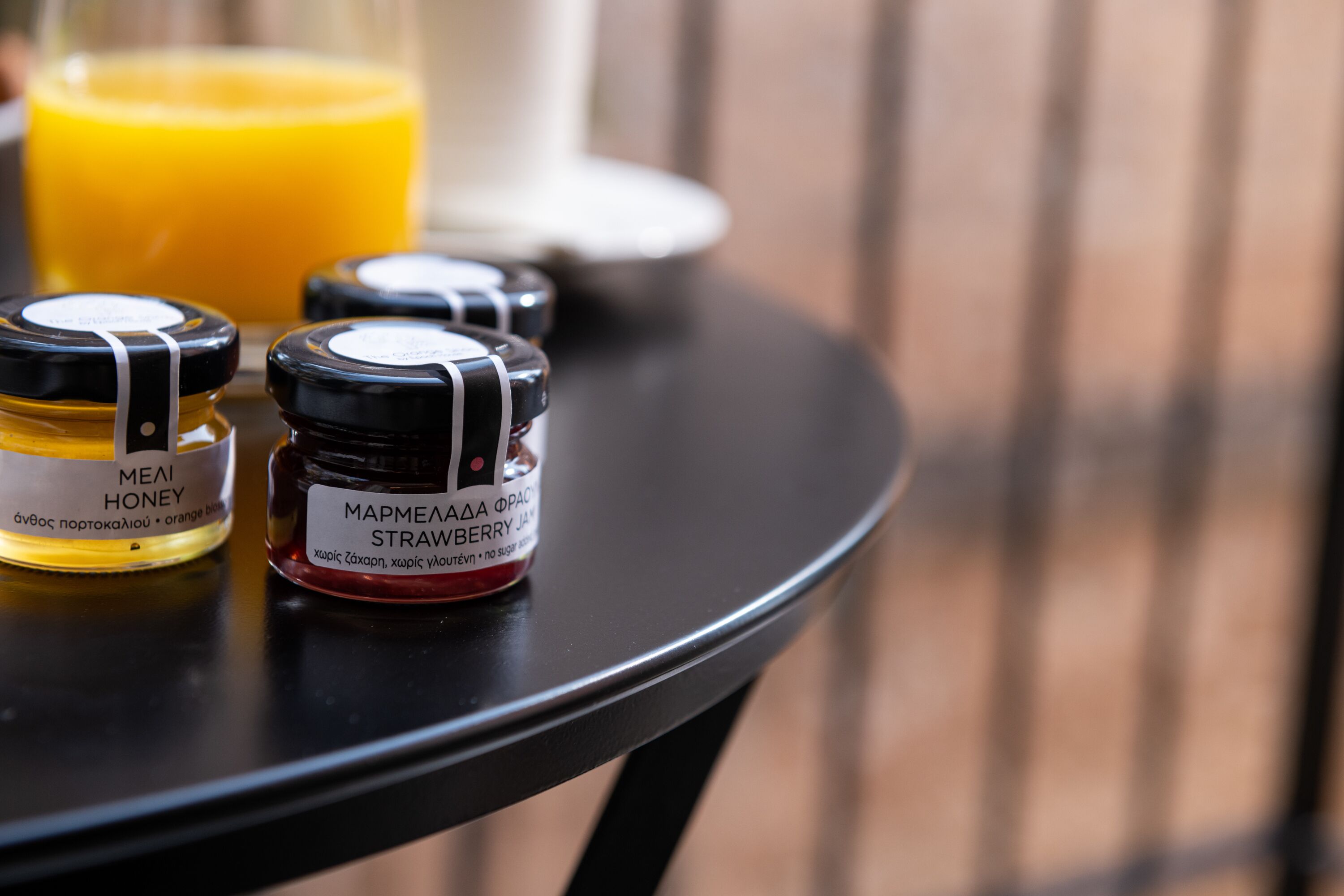 Two honey jars on a table with a glass of orange juice in the background.