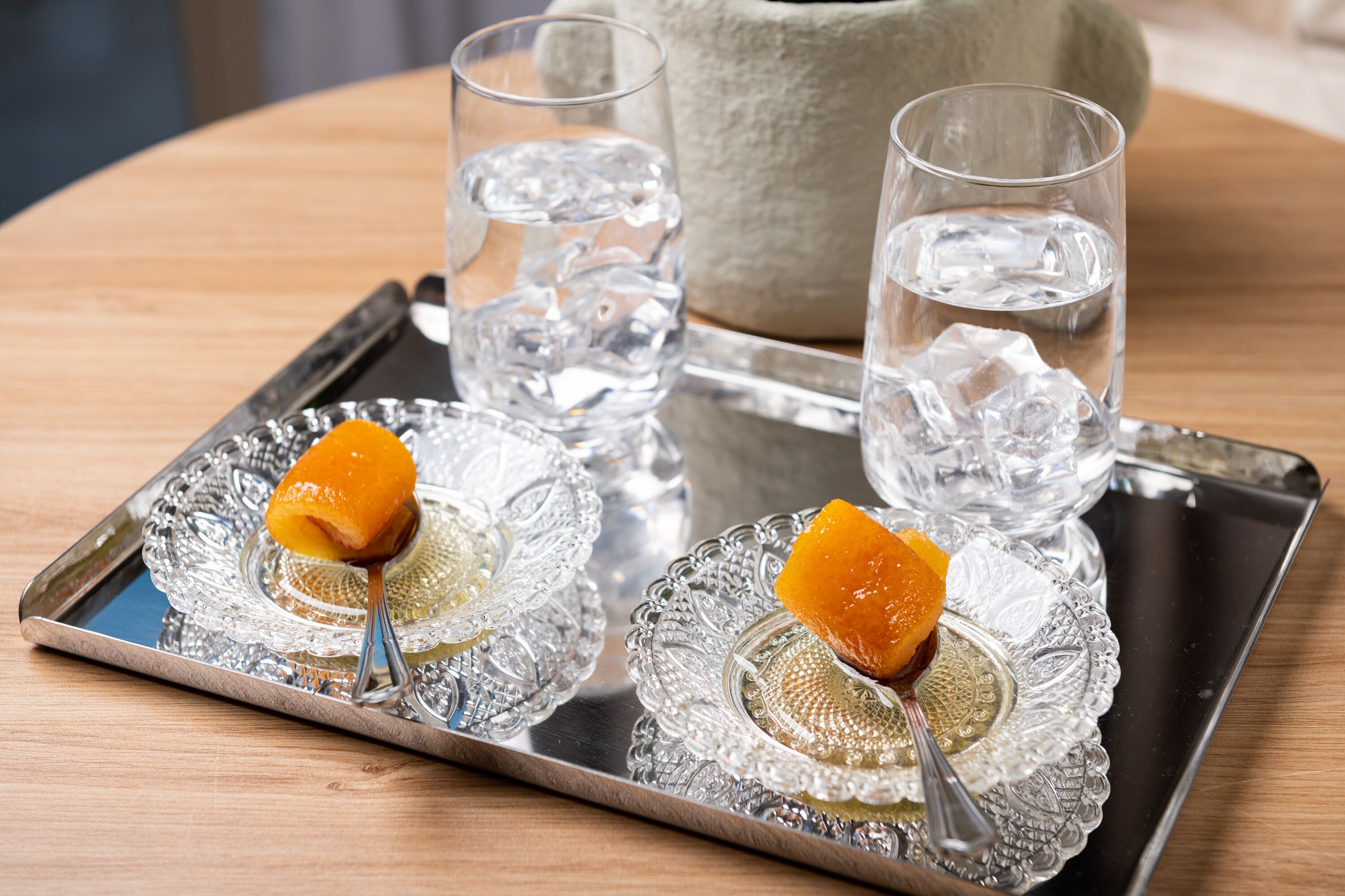 Een dienblad met twee glaasjes water en twee glaasjes met ijsblokjes en een oranje plakje op een houten tafel.