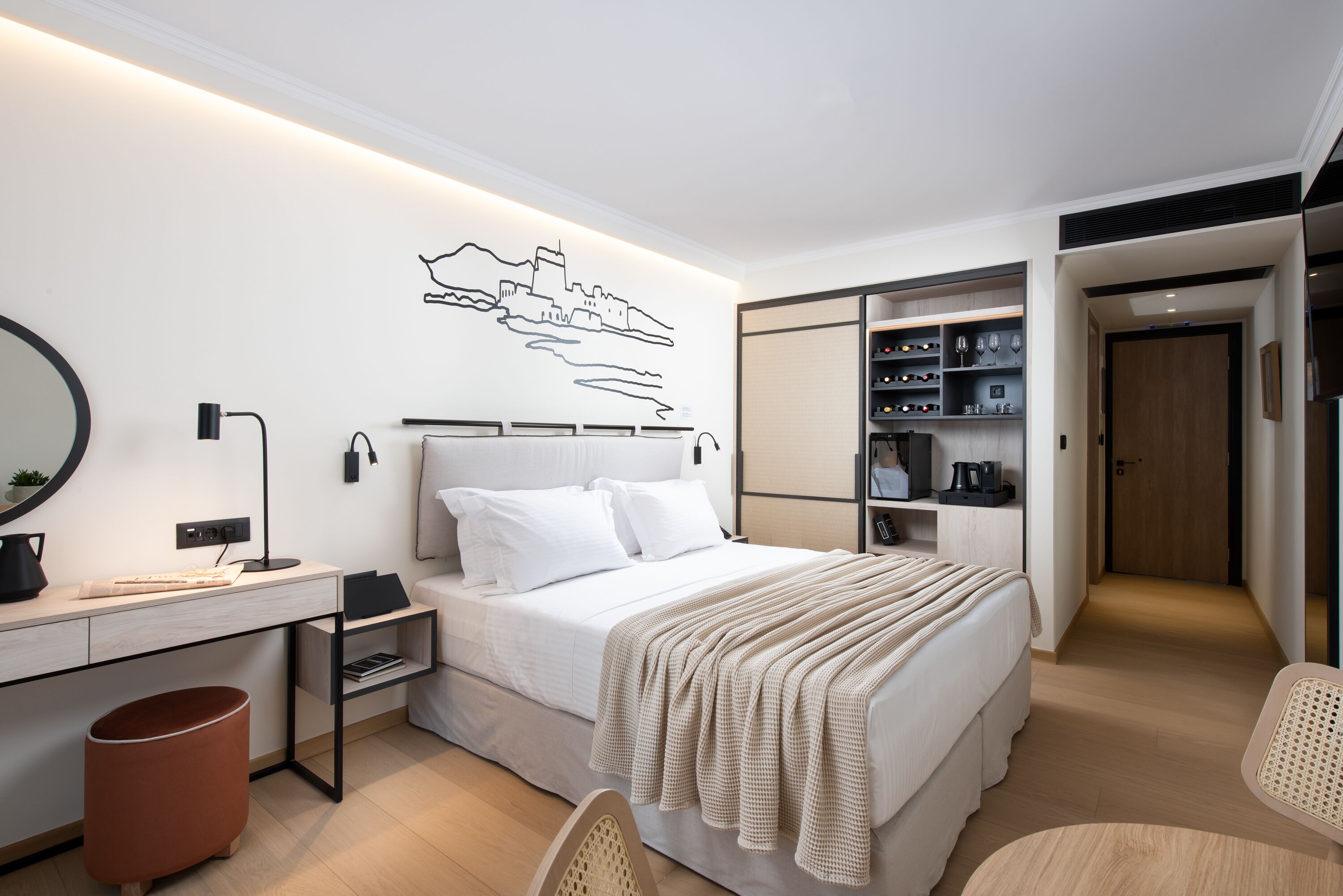 A modern hotel room with a neatly made bed, a desk with a computer, a chair, and a wardrobe.