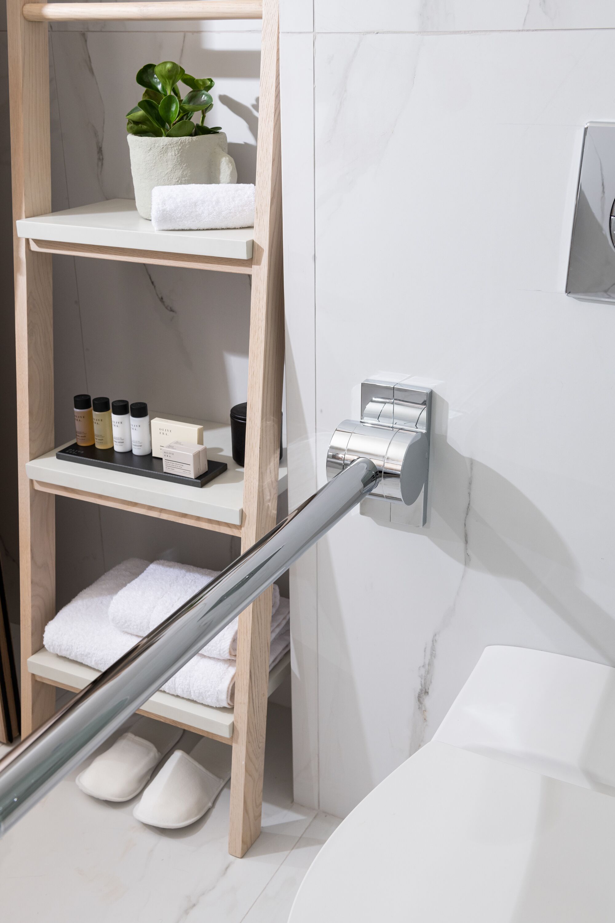 A bathroom with a wooden shelf holding towels, a potted plant, and toiletries.