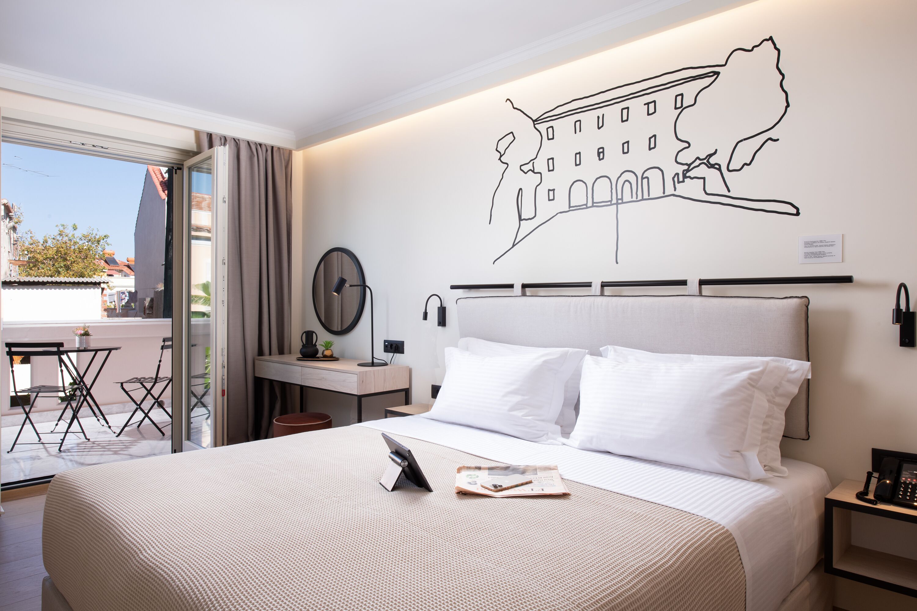 A hotel room with a bed, a desk, a chair, a table, and a view of the outside.