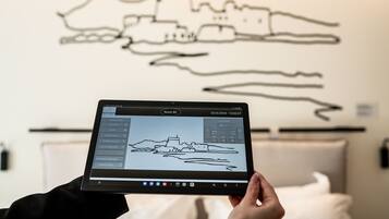 A tablet displaying a map of a coastal city with a castle, held in front of a wall with a similar outline.