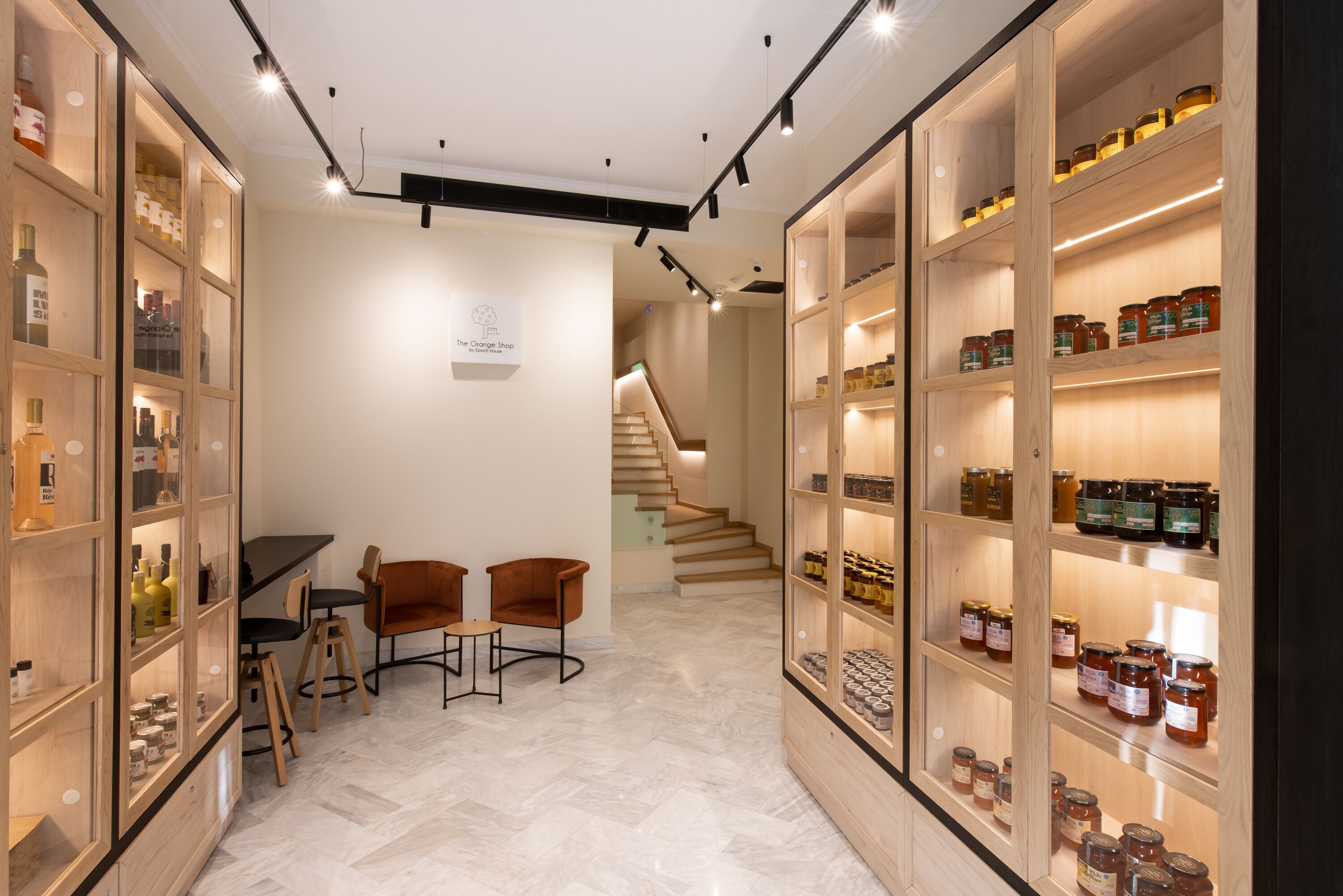 A modern interior with wooden shelving displaying jars, a staircase, and a small seating area.