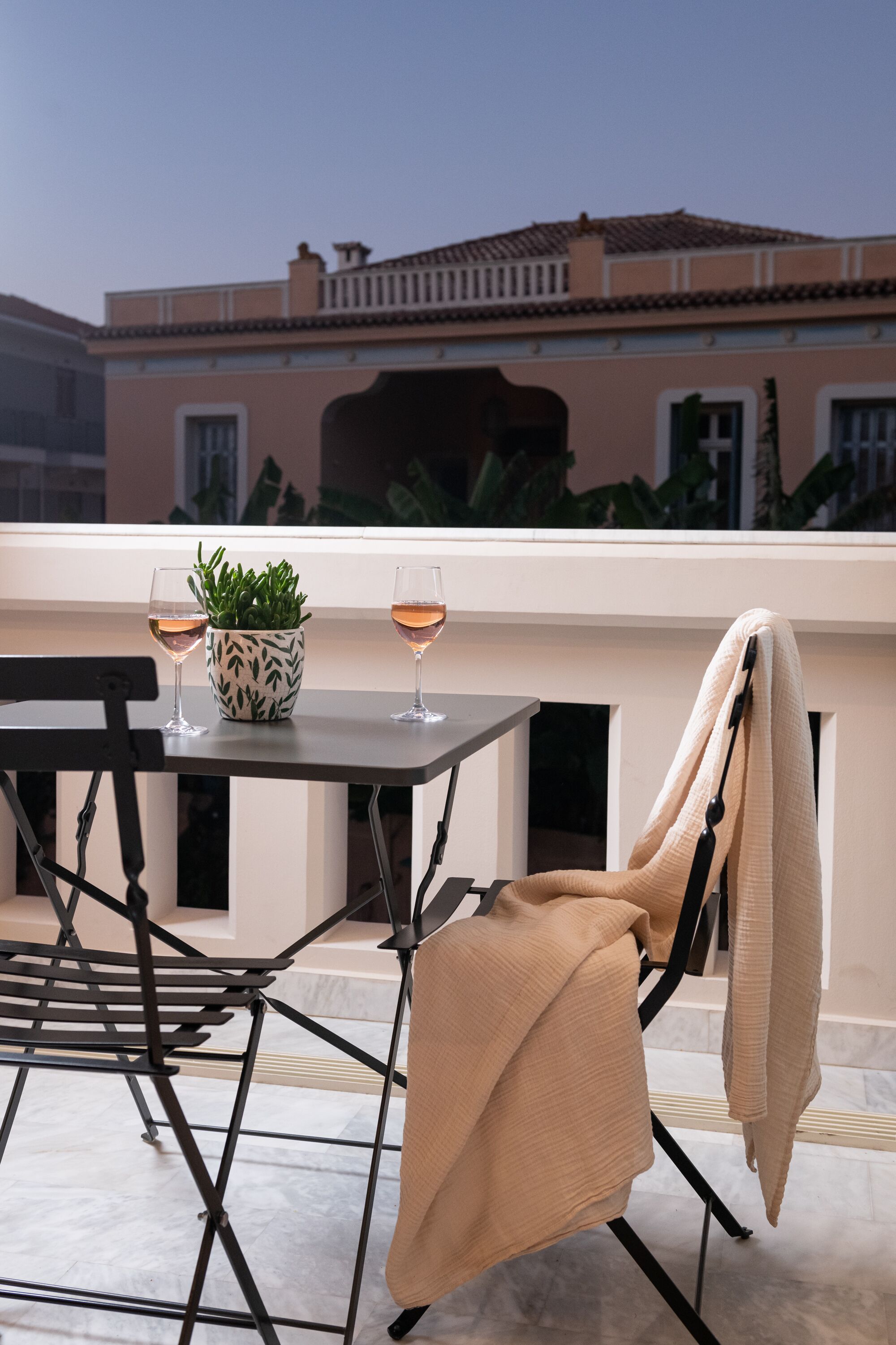 Une terrasse sur le toit avec une table, deux verres de vin, une plante en pot et une chaise avec une serviette.