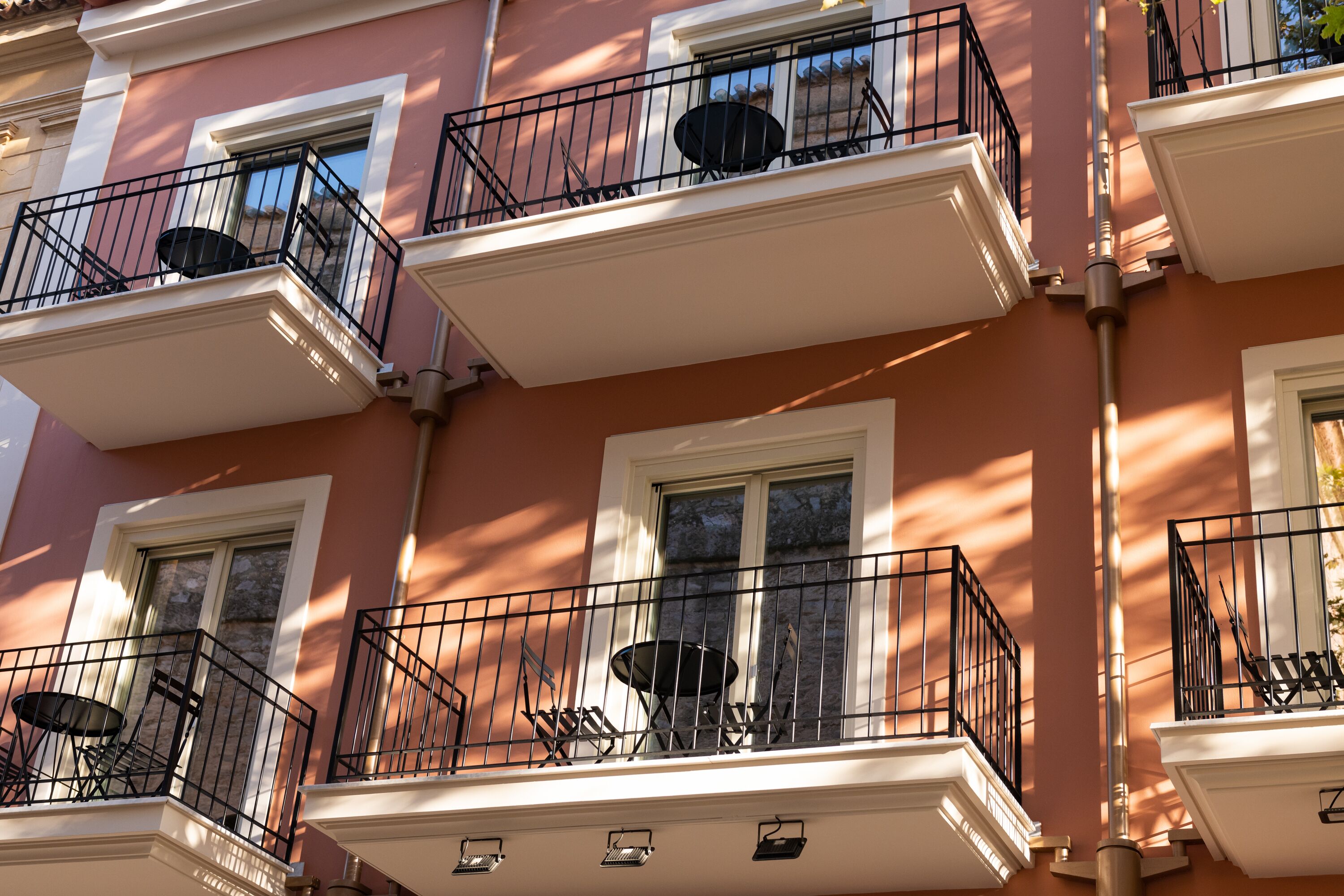 A multi-story building with balconies, each featuring a small table and chairs.