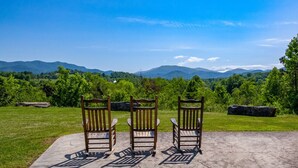Tres cadires de fusta orientades cap a una vista panoràmica de muntanyes i vegetació.