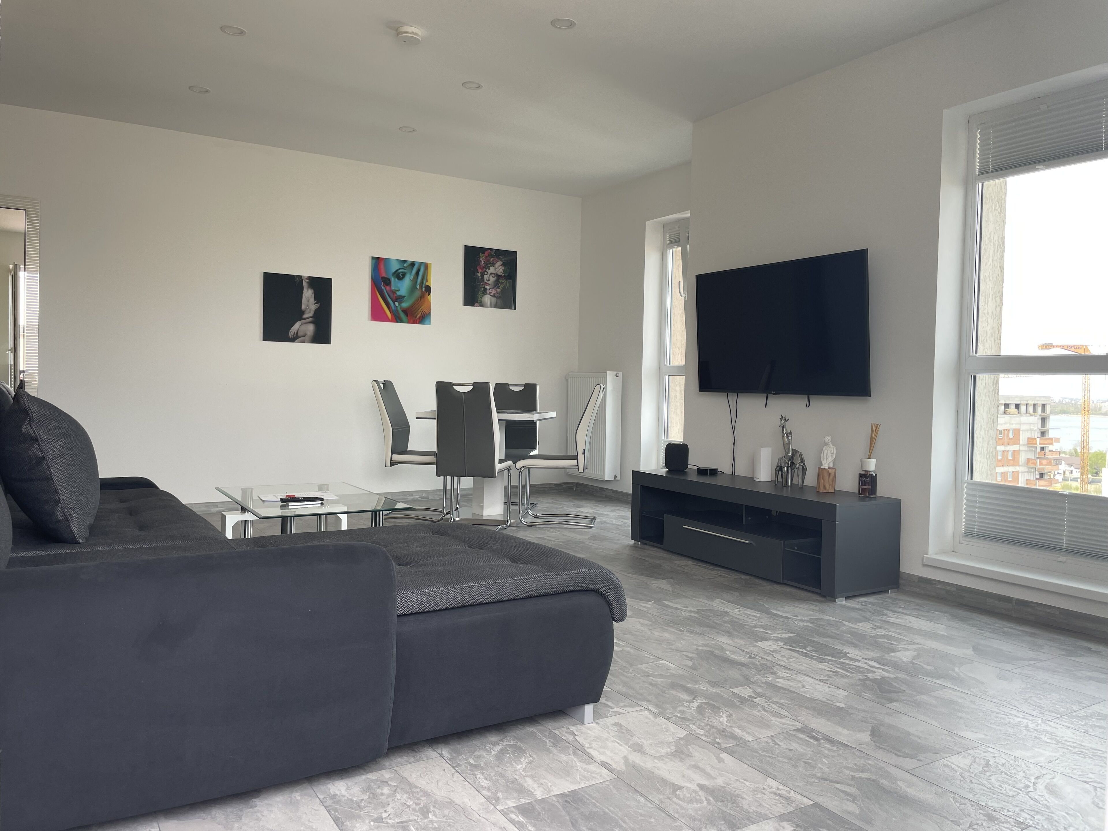 Ein modernes Wohnzimmer mit grauem Sofa, einem Glastisch, einem an der Wand montierten Fernseher und Kunstwerken an der Wand.