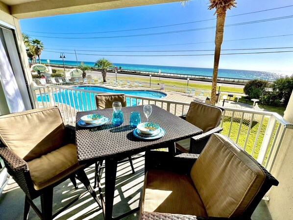 Un balcon avec une table dressée pour deux personnes, donnant sur une piscine et une plage.