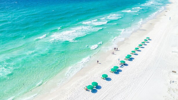 A beach with clear turquoise waters and a row of green umbrellas along the shore. - Luxury Gulf-Front 2BR 2BA Pet-Friendly Maravilla Resort Condo - Stunning Views (Miramar Beach)