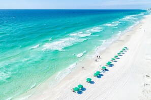 Een strand met helder turquoise water en een rij groene parasols langs de kust.